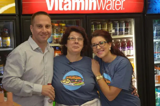 Rosa and Sonia with a visitor in front of the drink coolers